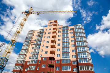 Tower crane  building new modern  apartment house on a background of blue cloudy sky at sunny day....