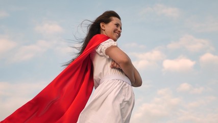 superhero girl standing on the field in a red cloak, cloak fluttering in the wind. close-up. girl dreams of becoming superhero. young girl in a red cape dream expression
