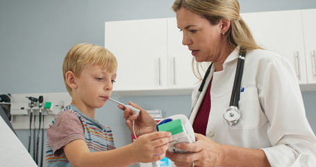Friendly female pediatrician using digital thermometer to check temperature of sick little boy. Child patient with a fever visiting doctor