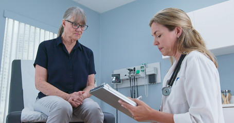 Female doctor taking medical history from older patient in exam room. Senior Caucasian woman...