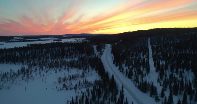 drone shot, following a vehicle, on a frozen route, between finnish woods and polar wilderness, in Pallas-yllastunturi national park, at the arctic circle, at sunset, on a sunny, winter evening dus