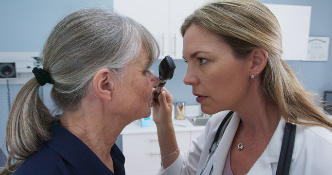 Close up of female doctor using ophthalmoscope to look into older patients eyes. Senior Caucasian woman visiting primary care physician for regular check up