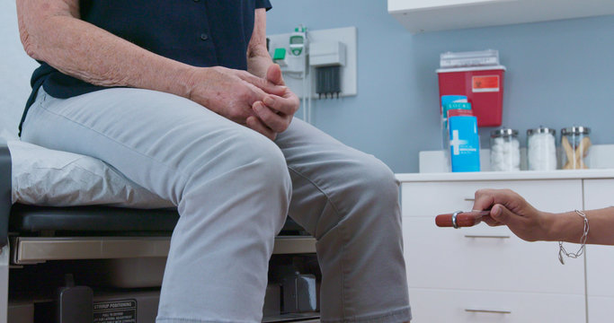Female doctor using reflex hammer to check older patients reflexes. Senior Caucasian woman visiting primary care physician for regular check up
