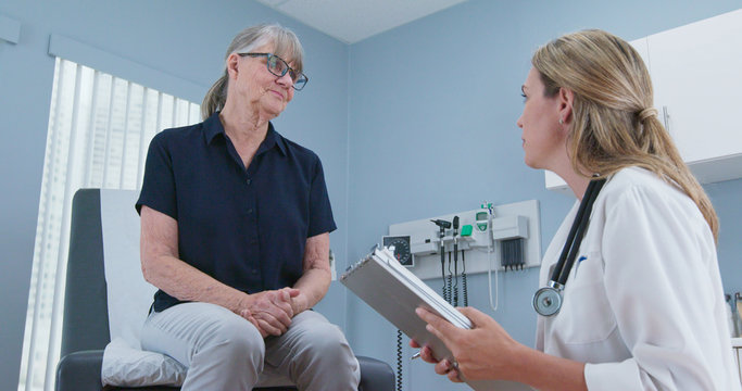 Female doctor taking medical history from older patient in exam room. Senior Caucasian woman visiting primary care physician for regular check up