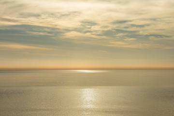 Obraz premium Golden morning on the sea. Golden morning on the sea. Calm horizon at sunrise, the rays are hiding in the clouds reflecting in the light path on the water.
