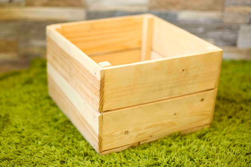 Empty wooden box on the green carpet against a stone wall background. Soft focus