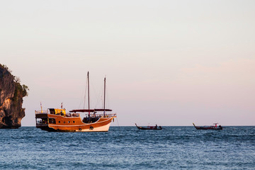 Fototapeta premium Sailing wooden ship in the old style sails on the sea. Nearby there are two small long-haul boats.