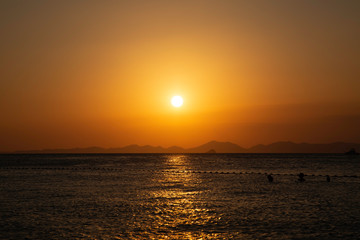 Golden sunset over the sea, mountain lines at background. People swimming in the water