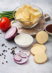 Fresh organic homemade potato crisps chips in glass bowl with sour cream and red onions on light kitchen table background. Tomato with ketchup and green onion
