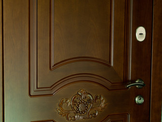 The entrance door to the house is brown with a pattern, handle and lock of gold color. The wooden door is of natural color.