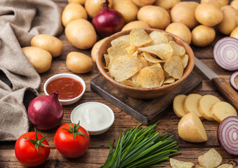 Fresh organic homemade potato crisps chips in wooden bowl with sour cream and red onions and spices on wooden table background. Fresh yellow potatoes with ketchup