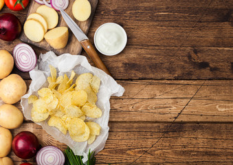 Fresh organic homemade potato crisps chips with sour cream and red onions and spices on wooden table background.Space for text
