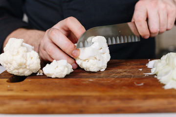 Chef cut raw cauliflower with knife. Kitchen. Wooden. Cook hands. 