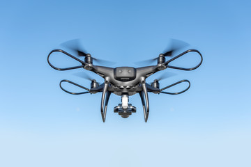 Dark drone flying through the air in the sun.