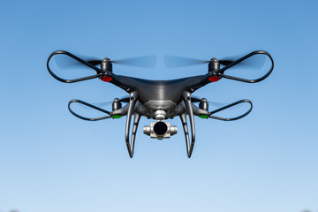 Dark drone flying through the air in the sun.