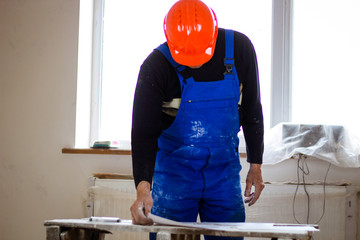 A builder in an orange construction catcher in his hands with drawings. Blue form combining. Repair...