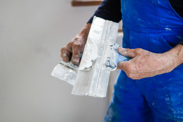 A builder in an orange construction cup in his hands with a spatula and a white putty. Blue form...