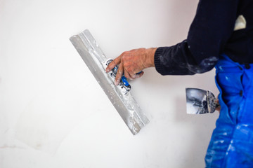 A builder in an orange construction cup in his hands with a spatula and a white putty. Blue form...