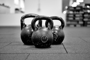 Naklejka na ściany i meble Тhree black iron kettlebells with markings 24 and 16 kg standing close to each other. Gym and fitness equipment. Workout tools. Black and white image