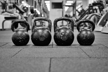 Naklejka na ściany i meble Тhree black iron kettlebells with markings 24 and 16 kg standing close to each other. Gym and fitness equipment. Workout tools. Black and white image