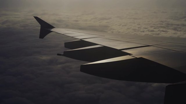 Wing of airplane flying above the clouds in the sky with sunlight
