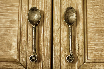 Ancient bronze handles wooden Cabinet in the form of spoons. Vintage cafe diner - detail close-up. Shabby retro style handles at the door in the kitchen