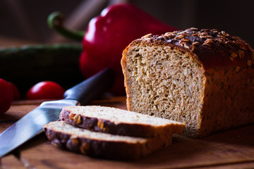 bochenek chleba, dwie kromki na desce na tle noża i warzyw