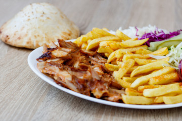 Chiken Doner Kebab on the plate with bread, french fries, tomatoes, onion, pickles and salad on a wooden background. Grilled chicken meat with vegetables.
