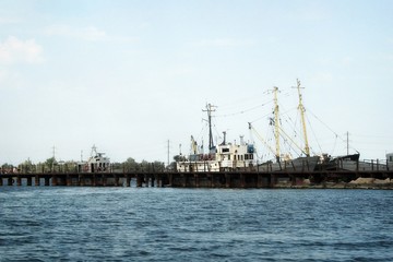 The old pier with rusty ships. Boats are at the broken pier. Repair docks with old bollards.