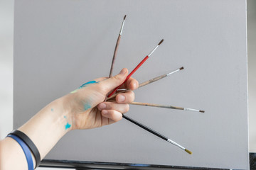 The girl artist holds different brushes for painting with oil paints on the background of a clean canvas.