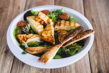 Grilled Halloumi Cheese salad witch tomatoes and lettuce in white plate in wooden background. healthy food
