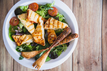 Grilled Halloumi Cheese salad witch tomatoes and lettuce in white plate in wooden background. healthy food