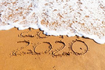 2020 year drawn on the sand being washed away by a wave on the beach