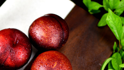 3 Red Plums close up shot with double colored cutting board and plum leaves in background 