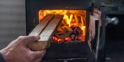 Man putting log to wood burning stove - obrazy, fototapety, plakaty