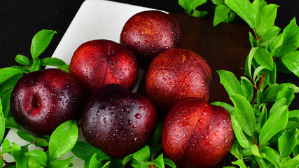 6 Red Plum arrangement with double colored cutting board and plum leaves in background 