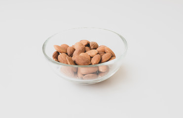 High angle view of raw almonds in glass dish on white background - matte effect and selective focus