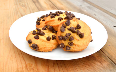 Freshly baked chocolate chip cookies in plate on wooden board