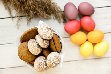 A cup filled with cookies is standing on a table beside a bunch of eggs and some wheat spikelets closeup.