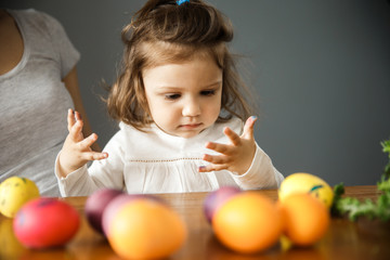 A young girl is painting on easter eggs with her mother. She is looking at her own dirty hands.