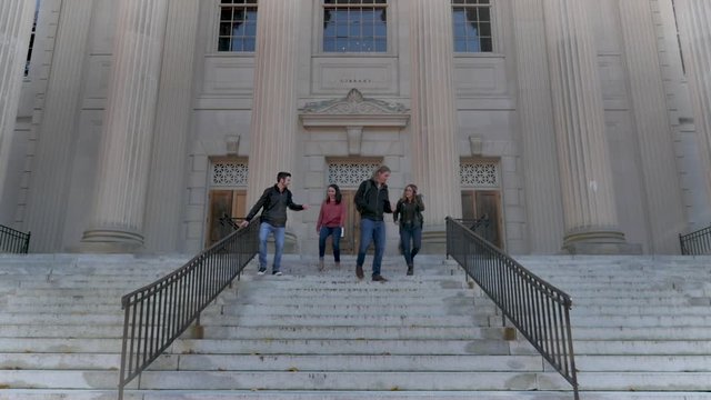 Four college university students walking down steps from a library