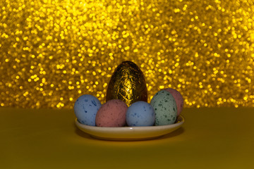 Golden egg on a golden background with defined bokeh, surrounded of colorful eggs