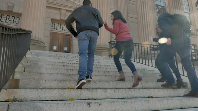 Four college friends walking up stairs towards a university library