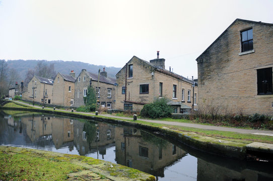streets of terraced houses alongside the rochdale canal in hebden bridge with buildings reflected in the water in winter