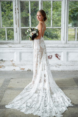 Beautiful bride poses in a luxurious long wedding dress with a bouquet in her hand and smiling
