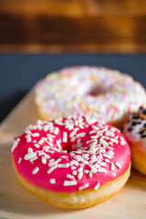 White, pink and brown glazed donuts on wooden background.