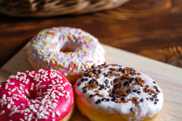 White, pink and brown glazed donuts on wooden background and near rattan basket .