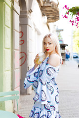 Beautiful blonde walks down the street with juice