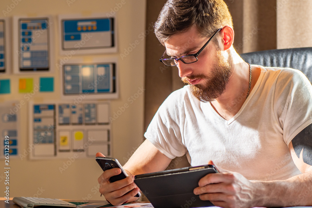 Poster designer working at new mobile applications. the designer compares the design of the site on the tab