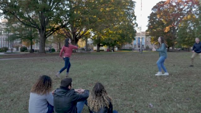 College friends playing frisbee together on a fall day on a university campus